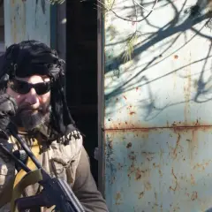 Hombre con turbante negro, gafas de sol y chaleco táctico, listo para una partida de milsim airsoft.